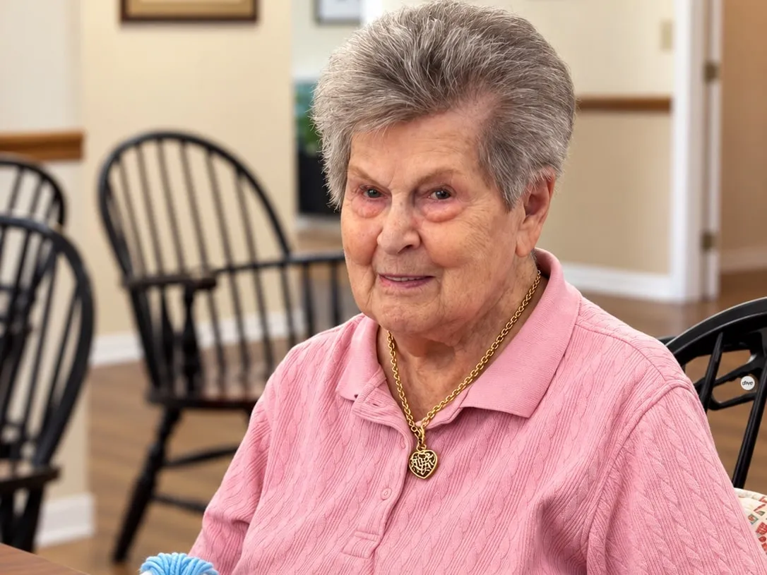 A smiling resident in a pink shirt sitting at the dining table