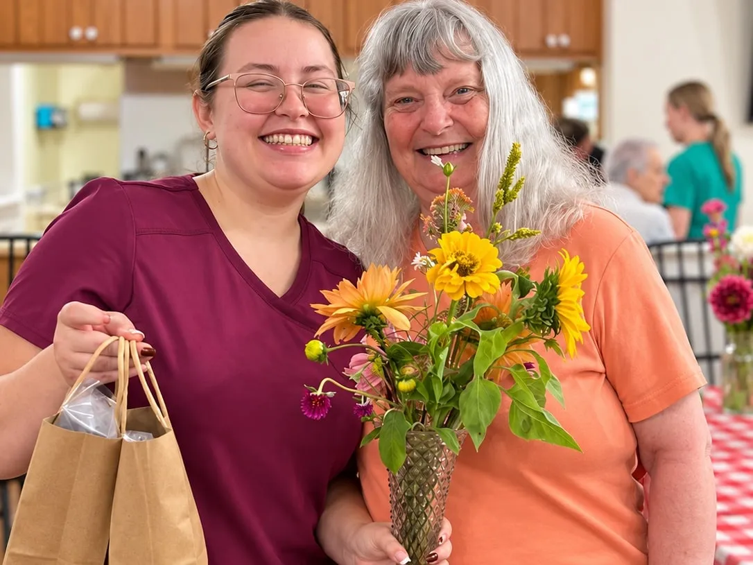 A staff member and a smiling woman holding a vase of fresh sunflowers