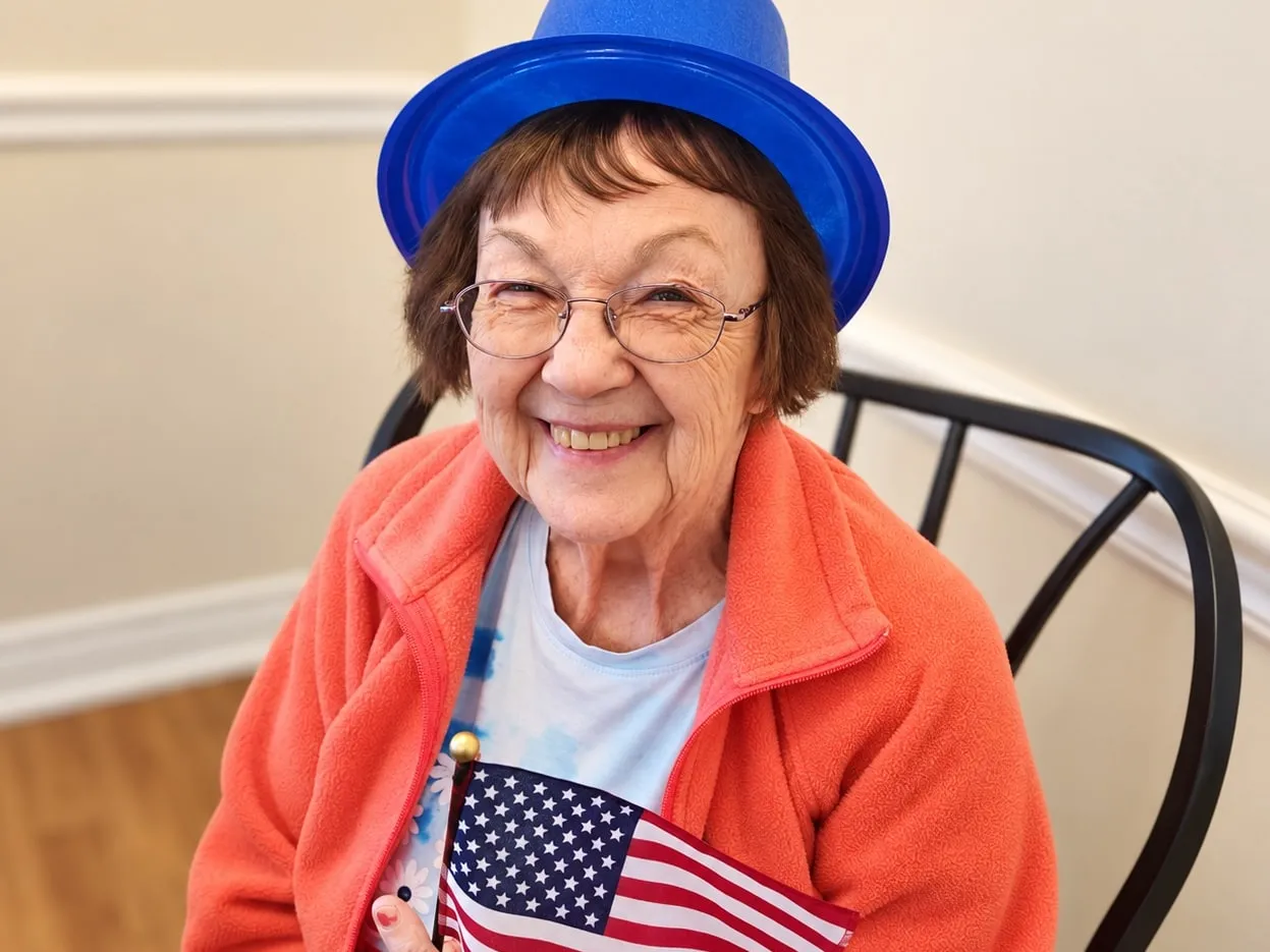 A smiling resident in a blue party hat holding a small American flag