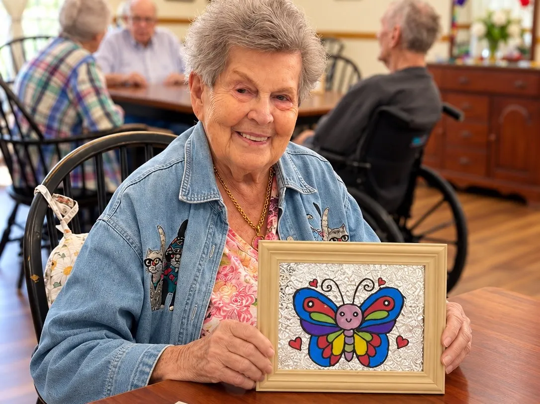 A resident showing her framed butterfly artwork in the dining room