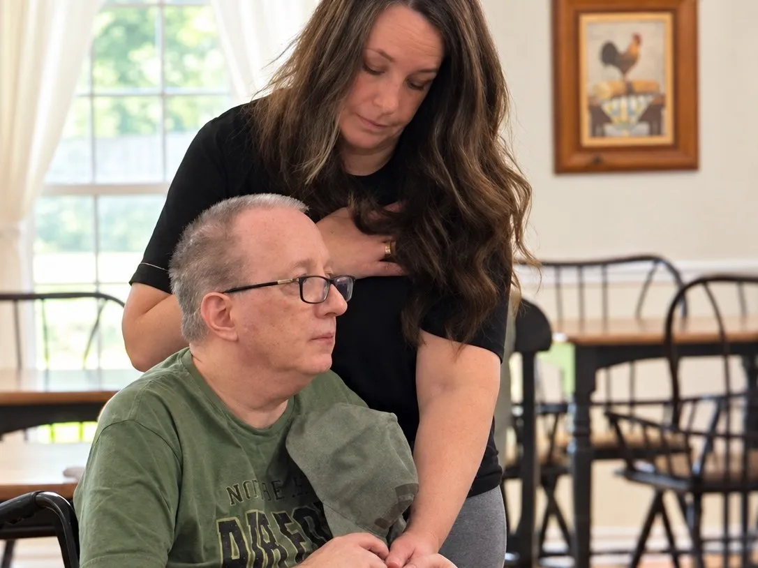 A caregiver resting her hands on a resident's shoulders as he sits in his wheelchair