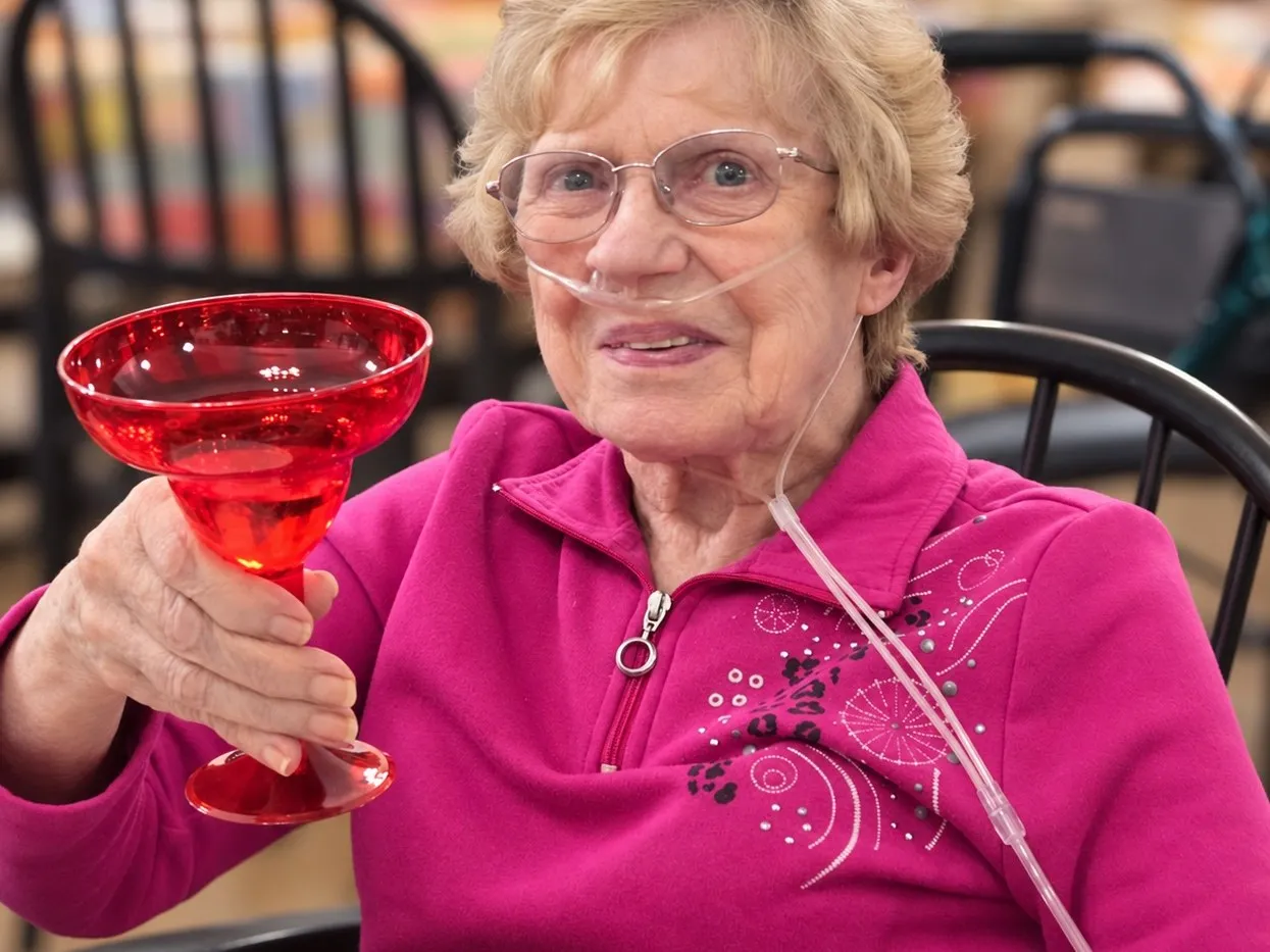 A resident in a pink sweater raising a red glass in a cheerful toast