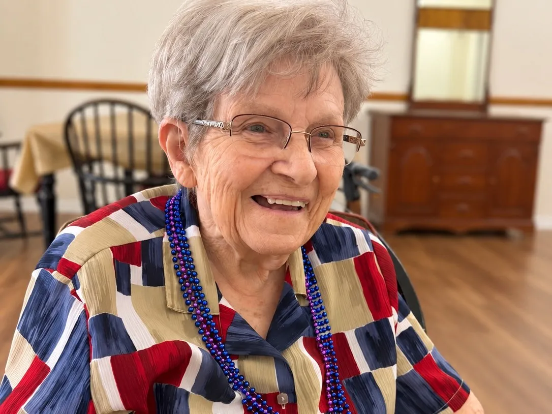 A smiling resident in a bead necklace enjoying her meal