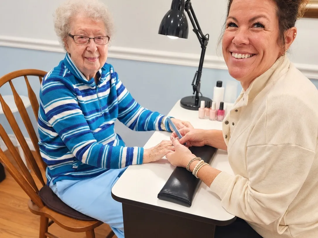 A resident in a striped sweater smiling while getting her nails done
