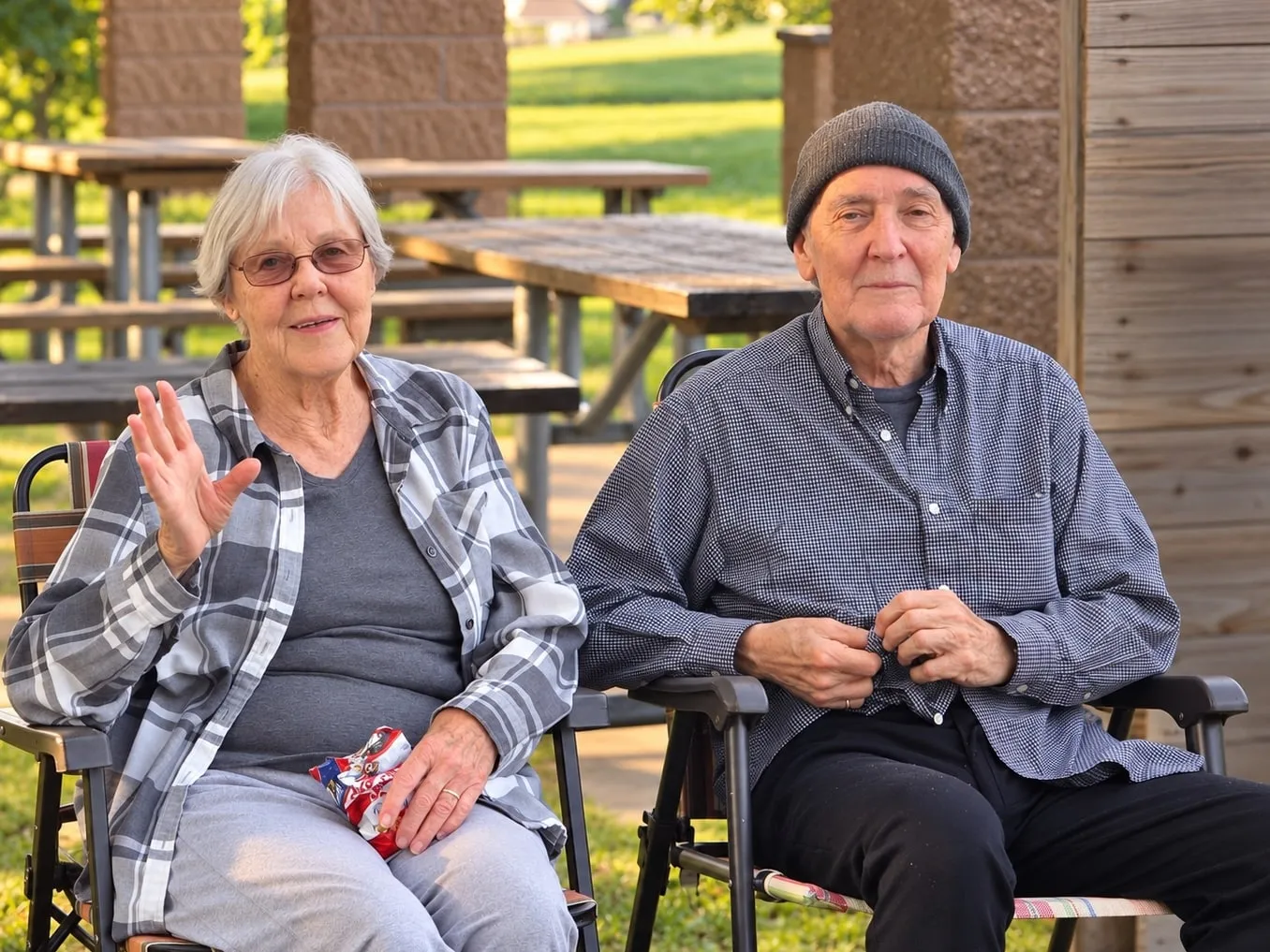 Two residents relaxing in chairs by the picnic tables, one waving