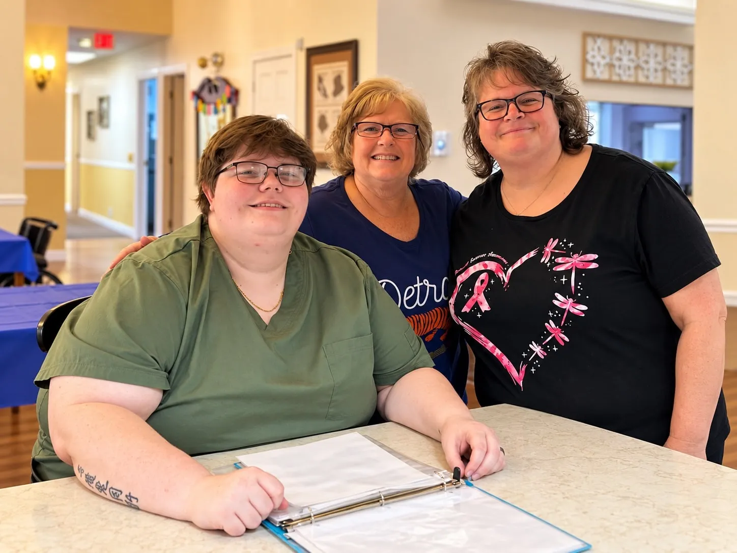 Three smiling women gathered around a table with a binder